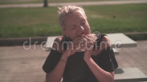 一个饥饿的金发女人在街上吃汉堡包年轻女子急切地吃着一个汉堡包手里拿着视频的预览图