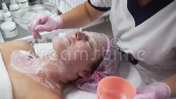 美容师在一名成年妇女的脸上涂上刷子的洁面乳视频的预览图