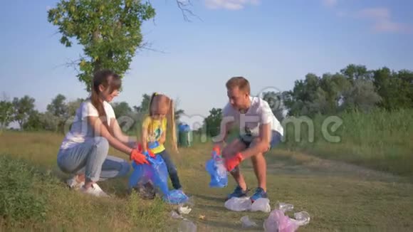 激进分子和小女孩在清理塑料垃圾时将垃圾收集在垃圾袋中的年轻幸福家庭画像视频的预览图