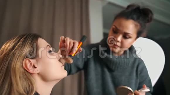 化妆的过程化妆师在模特脸上用刷子工作年轻金发美女的画像视频的预览图