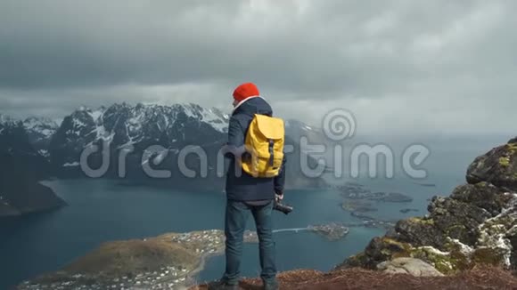 摄影师男带黄色背包站在山顶自然冒险旅行的概念挪威视频的预览图