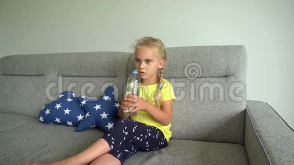 可爱的金发女孩坐在沙发上喝着瓶子里的水万向节运动视频的预览图