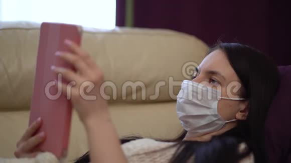 在检疫期间戴医疗面罩的妇女在家中使用片剂视频的预览图