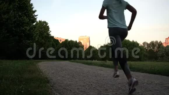 年轻的运动女子沿着绿色公园的灰色道路奔跑视频的预览图