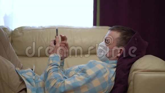 戴着医用口罩的人在隔离期间在家里使用智能手机视频的预览图