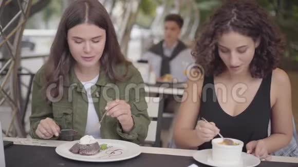 两个女孩坐在户外咖啡馆吃蛋糕的肖像女人用美味的甜点对待她的女朋友青年视频的预览图