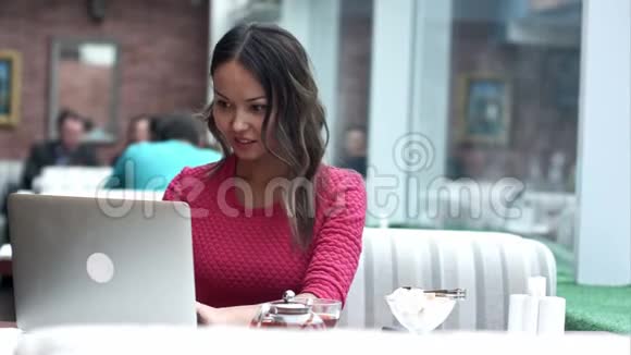 美丽的亚洲女人在现代咖啡馆里坐着便携式上网本梦想着什么视频的预览图