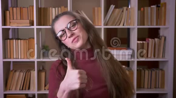 戴着眼镜的年轻白种人女学生的特写肖像拇指向上笑着欢快地看着镜头视频的预览图