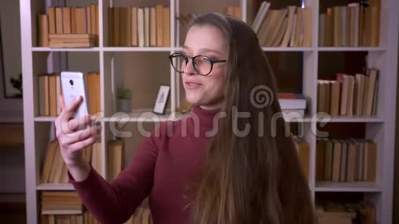 戴眼镜的年轻白种人女学生的特写镜头她在电话上打了一个视频电话在电话中愉快地交谈视频的预览图