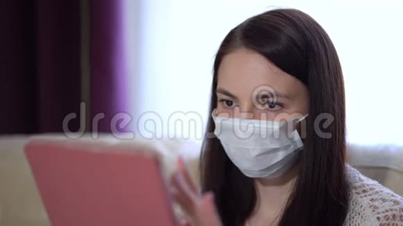 戴口罩的妇女在检疫期间在家中使用片剂视频的预览图