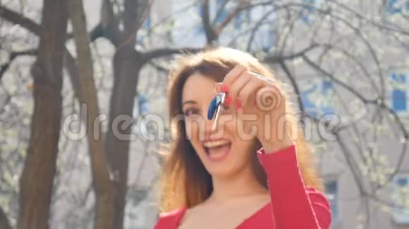 快乐的微笑的女人在春天的时候一只手拿着她的新公寓或汽车钥匙在户外用红色修剪视频的预览图