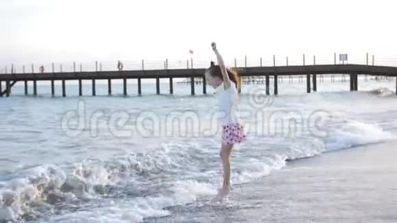 可爱的小女孩在海滩上日落时跳跃孩子喜欢在海边玩耍在水上嬉戏视频的预览图