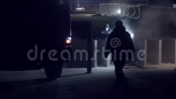 穿制服和防护绷带的城市工人夜间切割混凝土板磨床另一个人上了卡车道路视频的预览图