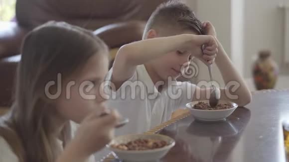 肖像可爱的妹妹和她疲惫的弟弟双胞胎试图吃粥或玉米片作为早餐没有欲望视频的预览图