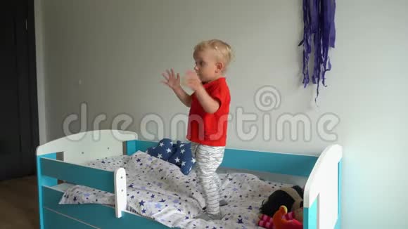 可爱的蹒跚学步的男孩在新床上跳跃幼儿拍手跑万向节运动视频的预览图