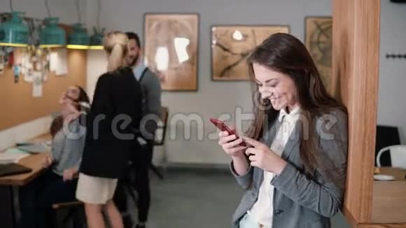 年轻漂亮的黑发女人在现代创业办公室里用触摸屏平板电脑嚼口香糖笑视频的预览图
