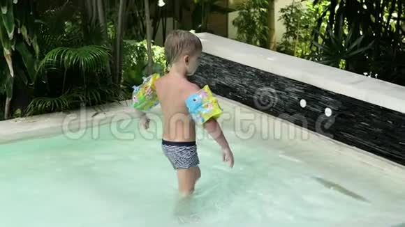 穿着袖子和帽子的小男孩在度假时跳进游泳池男孩在热带的游泳池里游泳儿童潜水视频的预览图