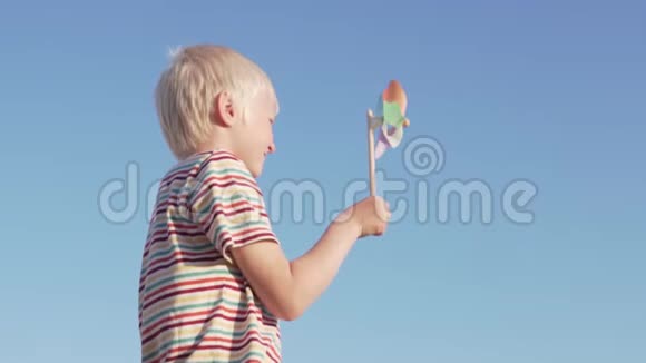 慢动作一个金发男孩一个旋转的风玩具快乐的微笑视频的预览图