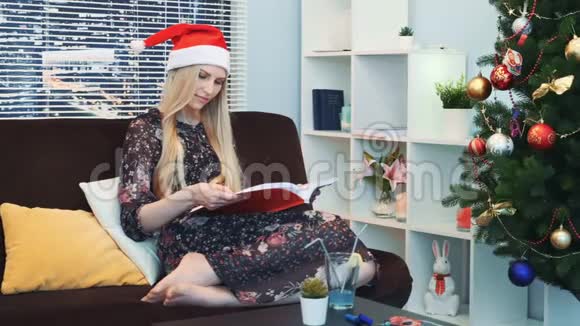 戴着圣诞帽的聪明女人在家坐在沙发上专心看书视频的预览图
