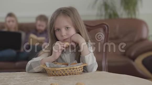 肖像可爱的小女孩吃饼干坐在桌子旁看着相机年轻时模糊的身材视频的预览图