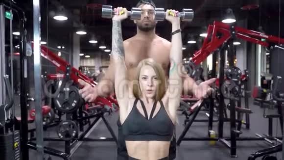 漂亮的健身女人和年轻的教练在健身房用哑铃举起手臂锻炼肌肉视频的预览图