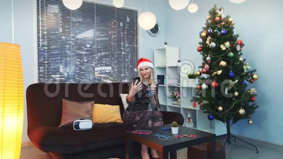 迷人的年轻女士用圣诞帽和饮料自拍视频的预览图