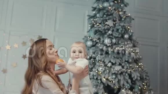 快乐的母亲在现代公寓的圣诞树附近亲吻可爱的孩子视频的预览图