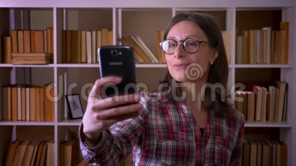 年轻漂亮的女学生戴着眼镜自拍在镜头前摆姿势的特写镜头视频的预览图
