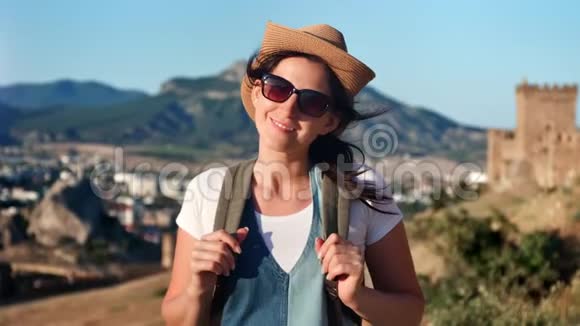 微笑的旅行妇女戴着太阳镜和帽子在群山环绕的城市里摆姿势视频的预览图