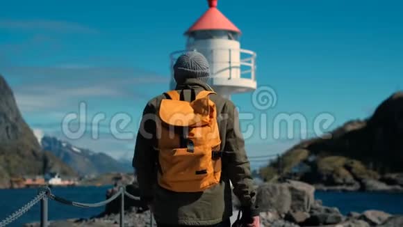旅行者带着一个黄色背包沿着风景如画的丘陵地带来到海洋附近的灯塔视频的预览图