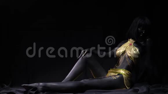 用黑色和金色的身体艺术拍摄年轻女子的照片正坐在地板上4K视频的预览图