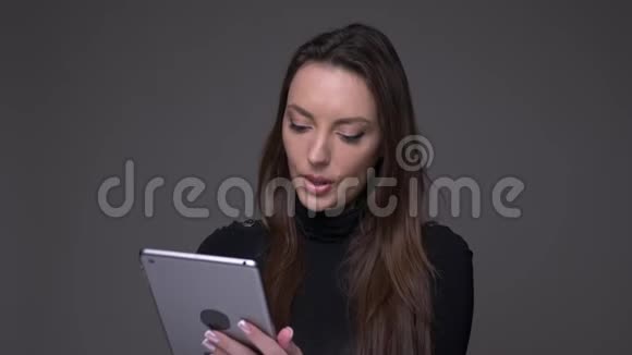 有吸引力的黑发女人与平板电脑一起工作的肖像是专注的集中在灰色背景上视频的预览图