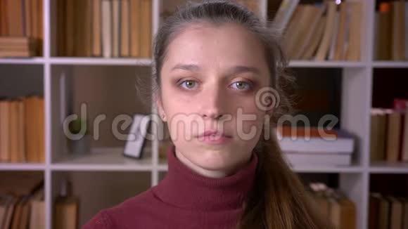一位年轻的白种人女学生在室内的unversity图书馆里看镜头的特写照片视频的预览图