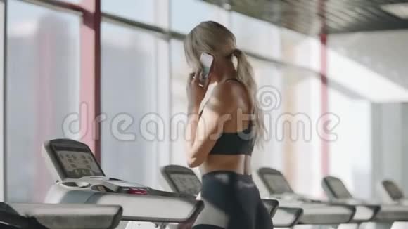 健身妇女在健身房的跑步机上行走打手机的美女视频的预览图
