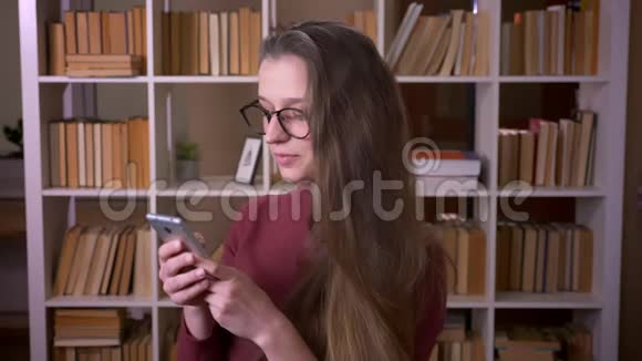 年轻的白种人女学生戴着眼镜在手机上浏览微笑着开心地看着镜头视频的预览图