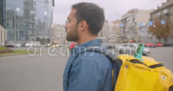 在城市户外带背包过马路的白种人成年送货员的特写侧景肖像视频的预览图
