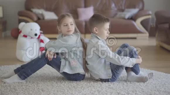 肖像双胞胎白种人男孩和女孩坐在客厅的地板上背对着对方生气兄弟和兄弟视频的预览图