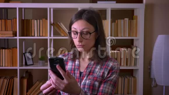 一位戴眼镜的年轻有魅力女学生的特写镜头她在室内的图书馆里打着电话视频的预览图