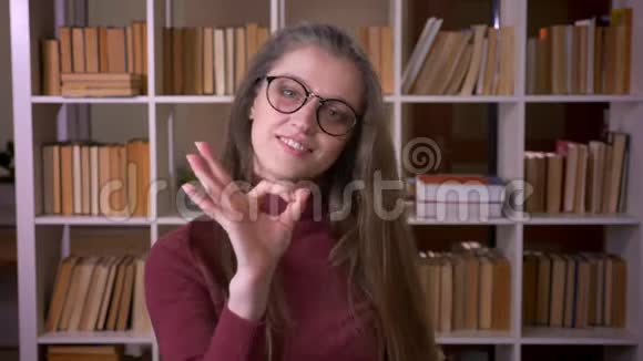 戴着眼镜的白种人年轻女学生的特写照片显示好的标志微笑着开心地看着镜头视频的预览图