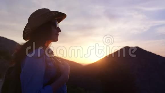 日落山背景下戴帽子戴太阳镜的可爱旅行女性剪影视频的预览图