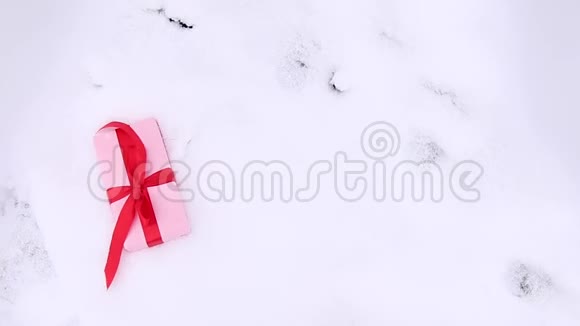 在雪地背景上用礼品纸和缎子红丝带包裹的坠落惊喜盒的俯视图视频的预览图