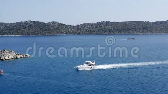 白色游艇在一个岩石岛附近的蓝色海面上航行视频的预览图