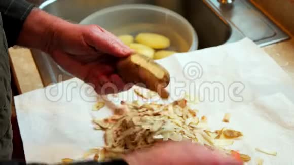 曼斯用橘色的削皮机剥土豆皮然后把成品土豆放入碗中放入厨房水槽中的水中作为一部分视频的预览图