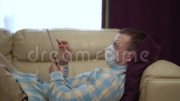 在检疫期间戴医疗面具的人在家里使用平板电脑视频的预览图