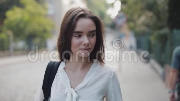 美丽的布鲁内特学生女孩带着一个袋子看镜头微笑的肖像年轻女子站在老城区视频的预览图