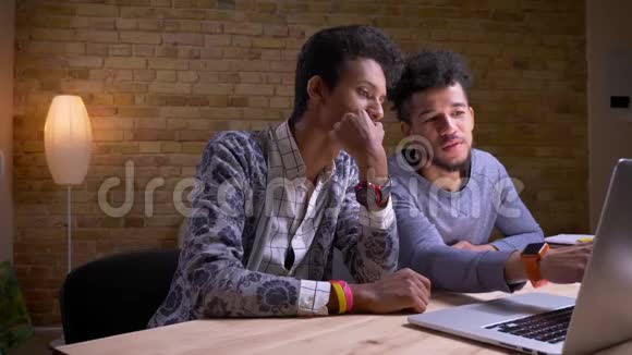 印度和非裔美国男学生使用笔记本电脑的特写镜头并笑着讨论一个项目视频的预览图