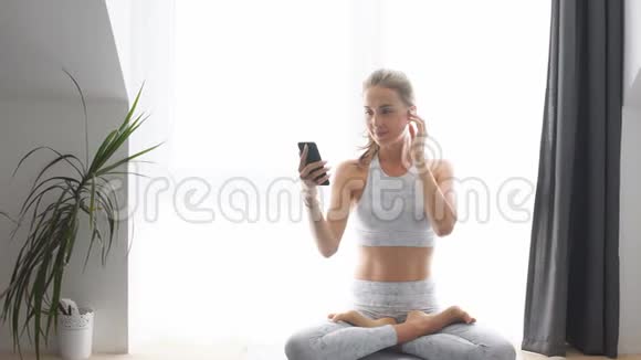 健身金发女郎戴着耳机准备早晨的普拉提视频的预览图