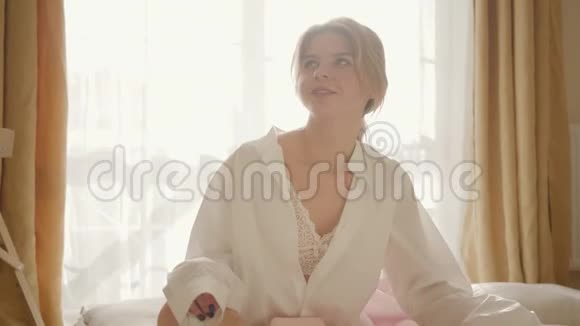美丽的金发白种人女人的肖像穿着蕾丝内衣和白色衬衫坐在床上微笑年轻漂亮视频的预览图