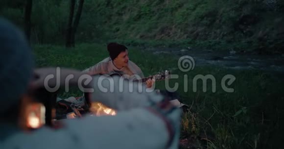 一个年轻人在一条山河附近的火堆前玩耍他的女朋友正在用照相机给他拍照视频的预览图