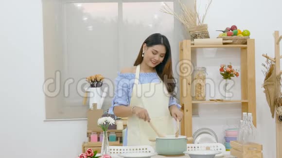 4K漂亮的亚洲女人在餐桌后面用勺子搅拌汤厨房里有锅菜和厨具视频的预览图